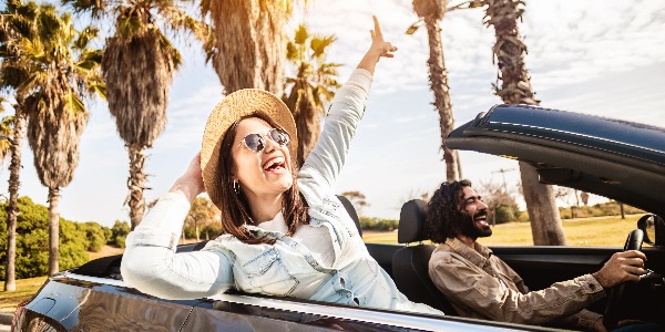 Happy young couple having enjoying summer vacation on convertible car - Man and woman laughing while driving a cabriolet auto outdoors - Travel, car rental service and holidays concept